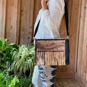 A woman standing in front of a wooden wall holding onto a bag.